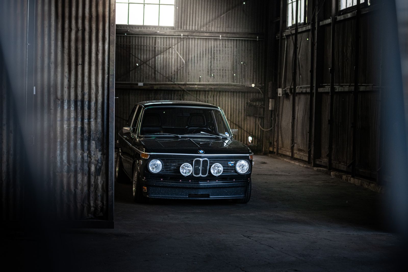 A black classic BMW parked inside a dim industrial garage